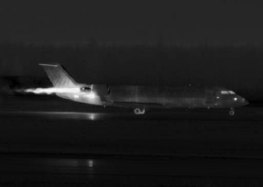 Aircraft on runway with visible thermal plume trailing from engines.